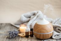 modern-aroma-oil-diffuser-wood-surface-with-knitted-element-candle-lavender-oil-blurred-background